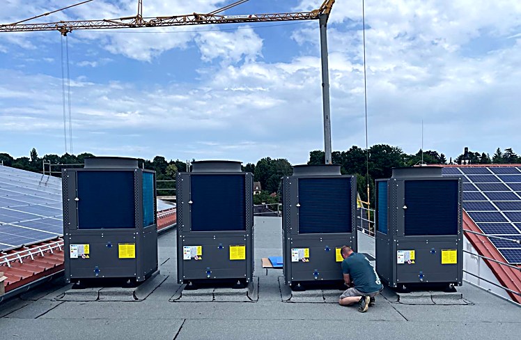Vier WP-HEATER-Außeneinheiten als Kaskade auf einem Flachdach in Zittau, Baukran im Hintergrund, Monteur bei der Inbetriebnahme